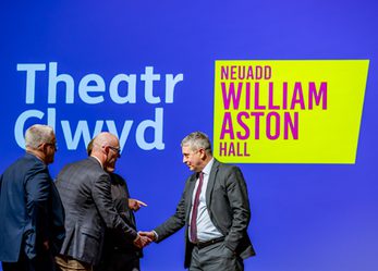 Men in suits, shaking hands in front of Theatr Clwyd and William Aston Hall logos.