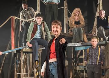 The cast of the play sit around on various bits of scaffolding.