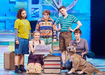 Group of 5 diverse children and a puppet dog on stage, looking at a map.