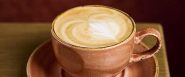 A Latte coffee in a salmon pink cup and saucer.