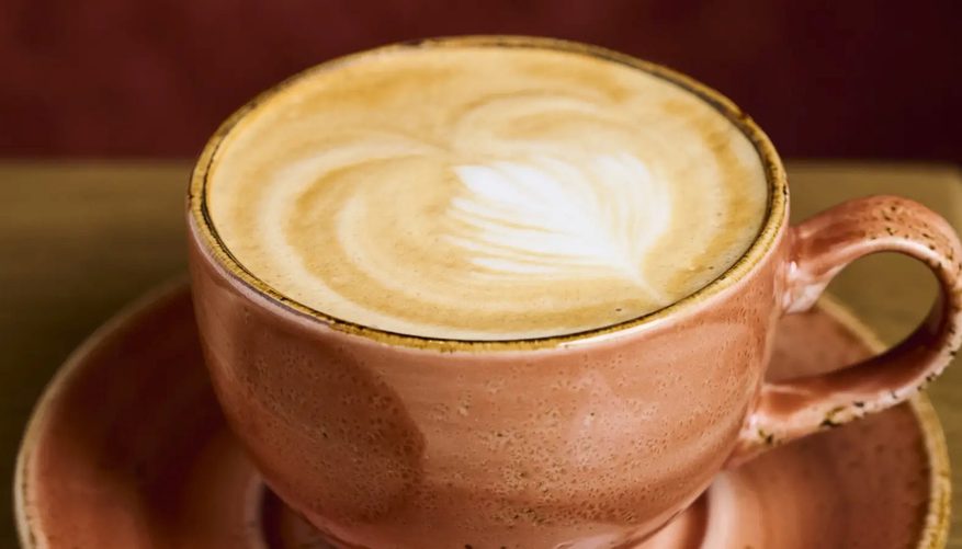 A Latte coffee in a salmon pink cup and saucer.