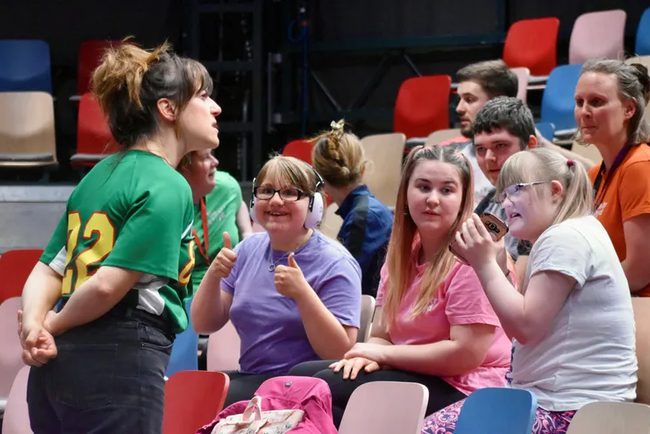 Diverse group of teenagers and young adults with additional learning needs sat in tiered theatre seating.